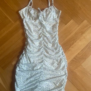 Blommig sommarklänning från H&M Divided - Söt ljusblå blommig klänning från H&M Divided med smala axelband och rynkade detaljer framtill. Klänningen har en figurnära passform och är perfekt för varma dagar. Tunt, mjukt material som känns skönt mot huden.