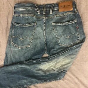 Blå Replay jeans med slitningar - Säljer ett par blå jeans från Replay med snygga slitningar och ljusare partier på benen. Jeansen har raka ben och normal passform. Ambass W32 L34