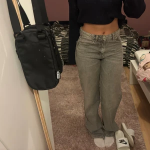 Gråa jeans  - Säljer ett par gråa jeans med hög midja och raka ben. Jeansen har klassisk femficksdesign och stängs med knapp och dragkedja. Perfekta för dig som gillar en clean och enkel look med lite vintage-vibe.