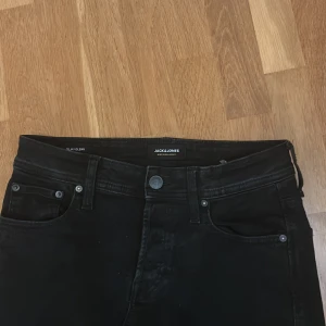 Svarta slim jeans Jack & Jones Glenn - Svarta jeans från Jack & Jones, modell Glenn. Storleken är 29/32. Slim fit med klassisk femficksdesign och knappgylf. Snyggt minimalistiska och passar perfekt till sneakers eller boots. Materialet är stretchigt jeans för skön passform.