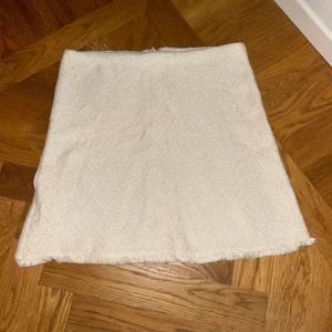 Vit kortkjol i strukturerat tyg - Säljer en vit kortkjol med råa kanter och strukturerat tyg. Kjolen har en enkel, rak passform och dragkedja bak. Perfekt för dig som gillar stilrena och minimalistiska plagg.