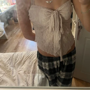 Ljusrosa spetsig linnetopp med knyt - Supersöt ljusrosa linnetopp med spets och knyt framtill. Toppen är ärmlös med smala axelband och har en feminin, croppad passform. Perfekt för varma dagar eller när du vill känna dig extra fin.