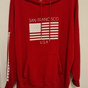 Röd hoodie från H&M - Röd hoodie från H&M. Tröjan har huva med snörning, känguruficka och vita stjärnor längs ärmarna. 