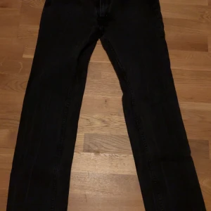 Svarta jeansbyxor från Acne, 32/34 - Svarta jeansbyxor från Acne i modellen Mic Raven. Klassisk femficksdesign med raka ben och snygga detaljer som silverfärgade nitar och Acne-läderpatch bak. Tillverkade i 100% bomull för en skön känsla och stilren look. Står att det är storlek 32/34 men skulle påstå att dem sitter som 30/32