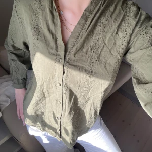 Olivgrön skjorta med broderade detaljer - Olivgrön skjorta med v-ringning och snygga broderade detaljer längs fram- och ärmar. Skjortan har knappar framtill och är långärmad. Tillverkad i ett lätt bomullstyg som känns luftigt och skönt. Perfekt för dig som gillar en chill och stilren look. Köpt på Zara i somras för 300, säljs för 200💞