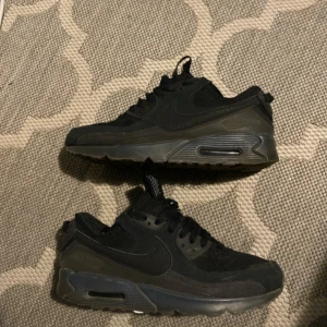 Nike Air Max 90 Triple Black, strl 42 - Säljer ett par helsvarta Nike Air Max 90 med klassisk chunky sula och synlig Air-enhet. Skorna har ovandel i mesh och syntet med snygga detaljer och svart swoosh på sidan. Perfekta för dig som gillar stilrena sneakers med streetkänsla.