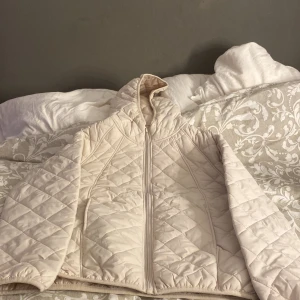 Beige quiltad pufferjacka med huva - Säljer en beige quiltad pufferjacka med huva och dragkedja framtill. Jackan har ett stilrent rutmönster och är tillverkad i syntetmaterial. Perfekt för kyliga dagar och har en skön, lite oversized passform. Aldrig använt! 💓