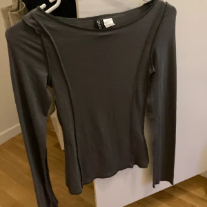 Mörkgrå långärmad topp från Gina Tricot - Säljer en mörkgrå långärmad topp från Gina Tricot i storlek XXS. Toppen har synliga sömmar längs framsidan och en något vid halsringning. Materialet är mjukt och stretchigt, perfekt för en stilren och enkel look.