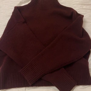 Vinröd polotröja från Zara - Mysig vinröd polotröja från Zara med ribbade muddar och hög krage. Tröjan är stickad och har lång ärm, perfekt för kyliga dagar. Enkel och stilren design som är lätt att matcha med olika outfits. Använd en gång.