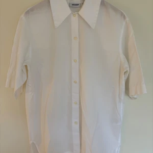Vit skjorta med kort ärm och oversized krage.från Weekday - Vit skjorta från Weekday med korta ärmar och oversized krage. Skjortan har rak passform, knäppning framtill och är tillverkad i bomull. Storlek XS. Perfekt skick!
