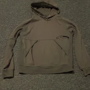 Grå hoodie från Sail Racing - Snygg grå hoodie från Sail Racing med huva och coolt Sail Racing-tryck på bröstet. Tröjan har långa ärmar, ribbade muddar och en stor magficka framtill. Perfekt för dig som gillar sportig och stilren look.