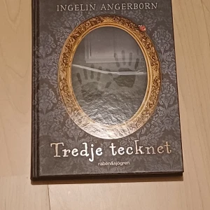 Tredje tecknet - En mystisk och spännande bok om Oliva som hittar en nyckel och märkliga saker börjar hända. Perfekt för dig som gillar mysterier, gåtor och lite kuslig stämning. Snyggt omslag med handavtryck och en gyllene ram – lockar till läsning!