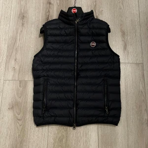 Marinblå dunväst från Colmar - Snygg marinblå dunväst från Colmar med horisontella sömmar och hög krage. Västen har två fickor med dragkedja och en diskret logga på bröstet. Perfekt för lager-på-lager och enkel att matcha med olika outfits.