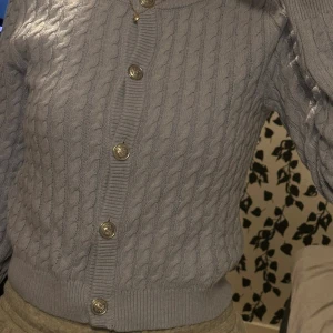 Ljuslila kabelstickad kofta med knappar - Supersöt ljuslila kabelstickad kofta från H&M med snygga silvriga knappar framtill. Koftan har rund halsringning, ribbade muddar och lång ärm. Perfekt att slänga över en topp för en chill och trendig look.