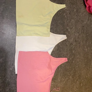 Tre ribbade one shoulder toppar - Säljer tre ribbade one shoulder toppar i olika färger: ljusgrön, vit och rosa. Alla ärmlösa och croppade med smal axelrem på ena sidan. Perfekta för sommaren och lätta att matcha med jeans eller kjol.