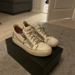 Giuseppe Zanotti skor - Snygga vita sneakers från Giuseppe Zanotti i skinn med beige detaljer på hälen. Skorna har snörning, dragkedjor på sidorna och en platt sula. Perfekta för dig som gillar exklusiva och trendiga sneakers med unika detaljer.