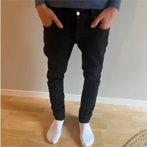 Jeans nudie  - Säljer ett par svarta skinny jeans från Nudie Jeans i storlek 30/32. Jeansen har klassisk femficksdesign, svarta sömmar och Nudie-logga på bakfickan. Snygg passform med smala ben och normal midja. Perfekta till en stilren och clean look.