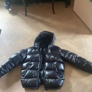 Svart pufferjacka från Zara - Säljer en svart, glansig pufferjacka från Zara. Varm och perfekt till vintern, finns inga täcken på användning. Ny pris 1400 kr. 