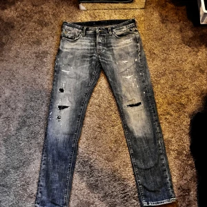 J&J jeans med skön fade och slitningar - Slim Glenn jeans i grått med slitna detaljer och hål på benen. Modellen är slim fit med smal passform och klassisk femficksdesign. Jeansen har en cool, tvättad look med ljusa partier och färgstänk för en trendig vibe. Skit nice nu till hösten!🍁