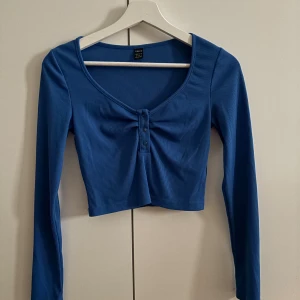 Blå långärmad topp - Säljer en croppad topp från Shein med lång ärm och ribbad struktur. Lite urringning i en fin blå färg. Perfekt för dig som gillar en enkel men snygg stil. Använd men inget slitage💙