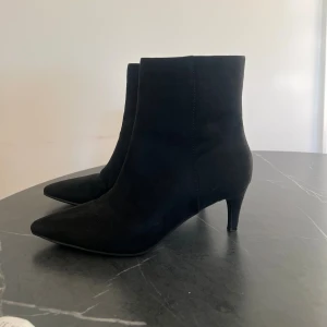 Svarta stövletter med spetsig tå - Svarta stövletter i mockaimitation med spetsig tå och smal klack. Skorna har dragkedja på insidan för enkel påtagning och en stilren, minimalistisk look. Perfekta för dig som gillar en clean och trendig stil. 
