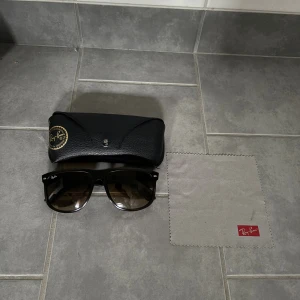 Svarta Ray-Ban boy friend solglasögon - Klassiska svarta Ray-Ban boy friend solglasögon med mörka glas och ikonisk logga på bågarna. Säljes med original svart fodral i läderlook och putsduk. Hör av er vid frågor!✌️🤩
