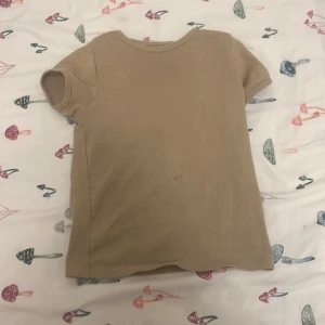 Beige ribbad t-shirt från 157 - En basic beige t-shirt från 157 i ribbad bomull. Modellen är kortärmad och har en enkel, rak passform. Perfekt för en clean och avslappnad stil.