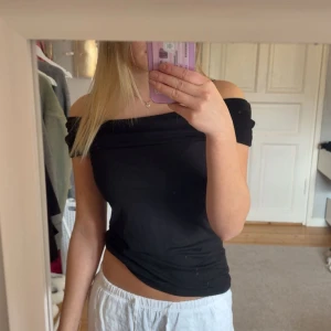 Svart offshoulder topp från Kappahl - Säljer en svart offshoulder topp från Kappahl i storlek S. Toppen har en snygg, åtsittande passform och ärmlös design med bred krage som vilar över axlarna. Perfekt för dig som gillar en stilren och enkel look. Materialet känns mjukt och stretchigt. Säljer då den är lite stor. Aldrig använd