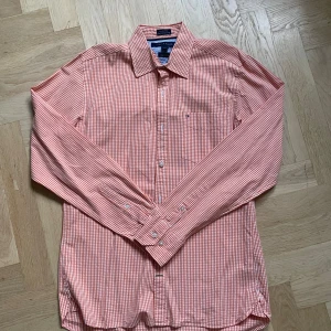 Rutig orange skjorta Tommy Hilfiger - Orange och vit rutig skjorta från Tommy Hilfiger i bomull. Klassisk krage, långärmad modell med knappar framtill och på ärmsluten. Custom fit och diskret logga på bröstfickan. Perfekt för dig som gillar färg och stilren design.