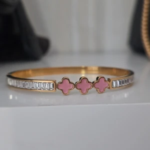 Guldigt armband med rosa klöver - Superfint armband i guldton med tre rosa klöverformade detaljer i mitten och gnistrande rektangulära stenar längs sidorna. Perfekt accessoar för att lyfta vilken outfit som helst med en söt och lyxig touch.