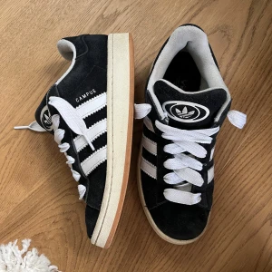 Adidas Campus svarta sneakers mocka - Svarta Adidas Campus sneakers i mocka med vita detaljer och klassiska tre ränder på sidorna. De är använda men är fortfarande i bra skick, lite smuts här och där men det går kanske att tvätta bort😊