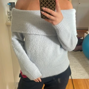 Ljusblå offshoulder stickad tröja - Supermjuk och fluffig ljusblå stickad tröja med offshoulder-design. Perfekt för dig som vill ha en mysig men ändå snygg look. Långa ärmar och bred krage som sitter snyggt över axlarna.