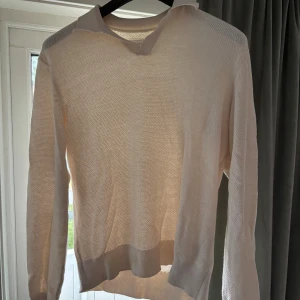 Ljusbeige stickad pikétröja - Säljer en ljusbeige stickad pikétröja med klassisk krage och v-ringning. Tröjan har lång ärm och är tillverkad i ett tunt, luftigt material som passar perfekt för lager-på-lager. Enkel och stilren design som funkar till många outfits.