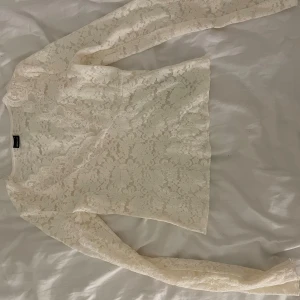 Vit spetsblus från Gina Tricot - Supersöt vit blus från Gina Tricot i spets med blommigt mönster. Långärmad och lätt transparent, perfekt för att lyfta en outfit. Sitter snyggt med en v-ringad halsringning och har en feminin känsla.
