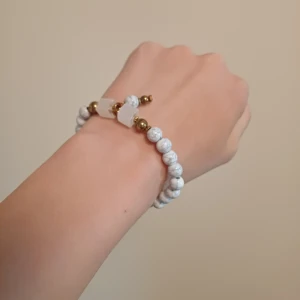 Vitt pärlarmband med guldiga detaljer - Stilrent armband med vita marmorerade pärlor och guldiga kulor. Armbandet har även två större vita stenar som ger en cool kontrast. Perfekt accessoar för att lyfta din outfit.