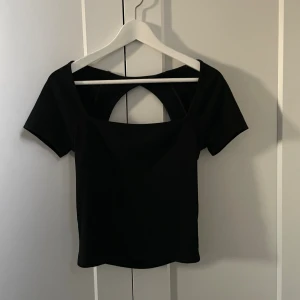 Svart topp med öppen rygg - Säljer en svart topp med korta ärmar och en snygg öppen rygg med rund utskärning. Toppen har en rak, croppad passform och i ett skönt material som inte sitter åt!