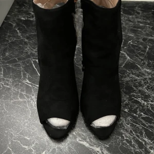 Svarta stövletter med öppen tå och klack - Snygga svarta stövletter i mocka-look med öppen tå och hög klack. Skorna har en stilren design med plattformsula och rundad öppning framtill. 