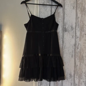 Svart Vila klänning  - Svart Vila klänning med volanger, knappar framtill och justerbara band. Storlek Large men skulle istället säga att det mer passar en Medium. 