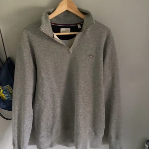 Grå half zip tröja från GANT - Säljer en stilren grå halv zip ifrån gant, nästan aldrig använd. Skriv vid funderingar eller prisförslag!