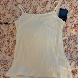 Vit ribbad linnetopp Brandy Melville - Supersöt vit linnetopp från Brandy Melville med tunna axelband och diskret ribbat mönster. Materialet är mjukt och väldigt stretchigt. Aldrig använd. 