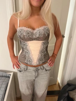 rosa spetskorsett - Säljer en snygg korsett i rosa och grått med blommig spetsdetalj och justerbara axelband. Toppen har en v-ringad form framtill och stängs med hakar i ryggen💝