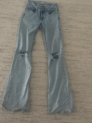 Bootcut ljusblå jeans från Nelly  - Ljusblåa utsvängda jeans från Nelly med hål på knäna, super fina säljer för att de är för korta för mig