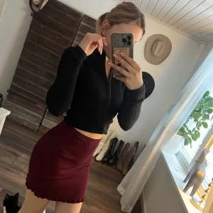 Vinröd kortkjol med volangdetalj - Snygg vinröd kortkjol med volangdetalj i nederkant. Perfekt för att ge en touch av stil till din outfit. Kjolen har en tight passform som framhäver figuren.