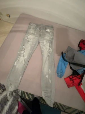 Dsquared2 ljusgrå skinny jeans - Säljer ett par ljusgrå skinny jeans från Dsquared2 med slitna detaljer och coola färgstänk. Jeansen har dragkedja, fem fickor och klassisk Dsquared2-tag baktill. Perfekt för dig som gillar streetstyle och vill sticka ut med en edgy look.
