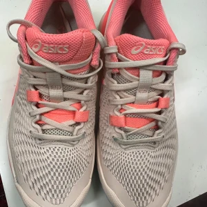 Asics sneakers i ljusrosa och korall - Snygga Asics sneakers i mesh och syntet med ljusrosa och korallfärgade detaljer. Skorna har snörning, rund tå och platt sula med mönstrad undersida för extra grepp. Perfekta för träning och sport, med ventilerande material och cool design.