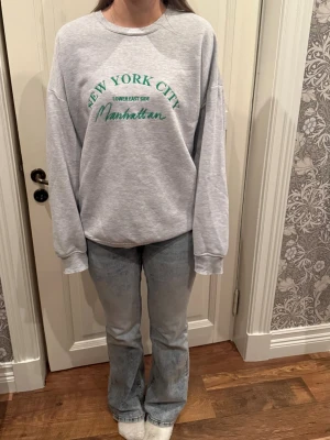 Grå sweatshirt med text - Grå sweatshirt med grön text ”New York City”, längre än vanlig passform 