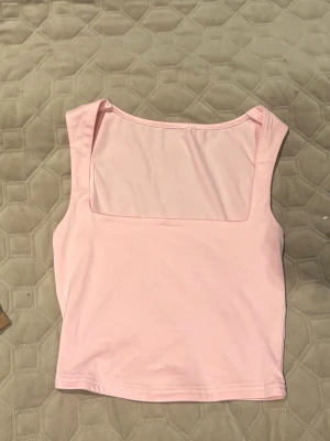 Ljusrosa ärmlös linnetopp - Säljer en ljusrosa linnetopp med fyrkantig halsringning. Toppen är croppad och har en enkel, stilren design utan mönster eller detaljer. Perfekt för varma dagar och enkel att matcha med jeans eller kjol.