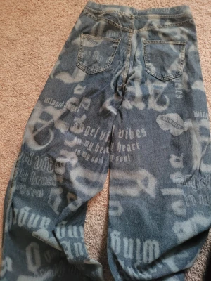 Blå wide jeans med tryck från ONLY - Säljer ett par blå jeans från ONLY i storlek 146 med coolt blekt tryck och text över hela byxorna. Modellen är wide och har två bakfickor. Byxorna har en avslappnad passform, strechiga som ger en skön streetkänsla.