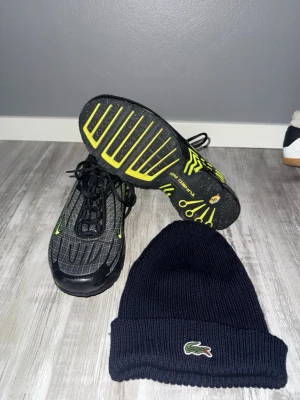 Nike TN Skor + Lacoste mössa - Nike TN Skor i svart och grått med limegröna detaljer och mönstrad ovandel.  Mycket bra skick, den är använd ungefär 2-3 gånger. Du får med en mörk blå lacoste mössa på köpet helt gratis 