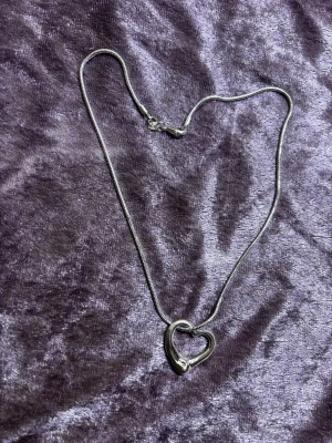 Silverpläterad ( stämplad) hjärtformad halskedja - Säljer en stilren halskedja i Silverpläterad med ett öppet hjärta som hänge. Kedjan är tunn och smidig, och hänget har en modern, mjuk form. Stämplad med 925 vilket indikerar äkta silver. Perfekt för dig som gillar minimalistiska smycken. Helt ny 